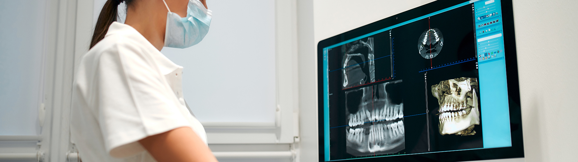 A person is seated in a dental chair, receiving care from a dental professional who stands behind them.