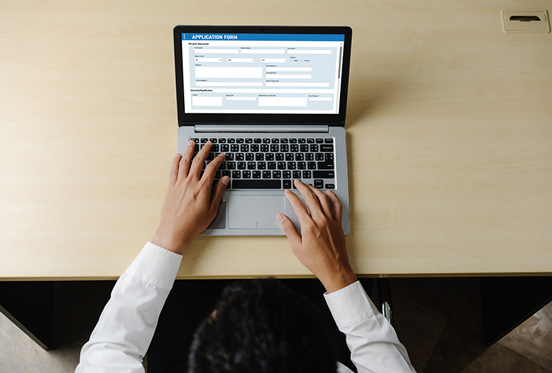 A person using a laptop computer with a screen displaying a form, suggesting an online registration process.