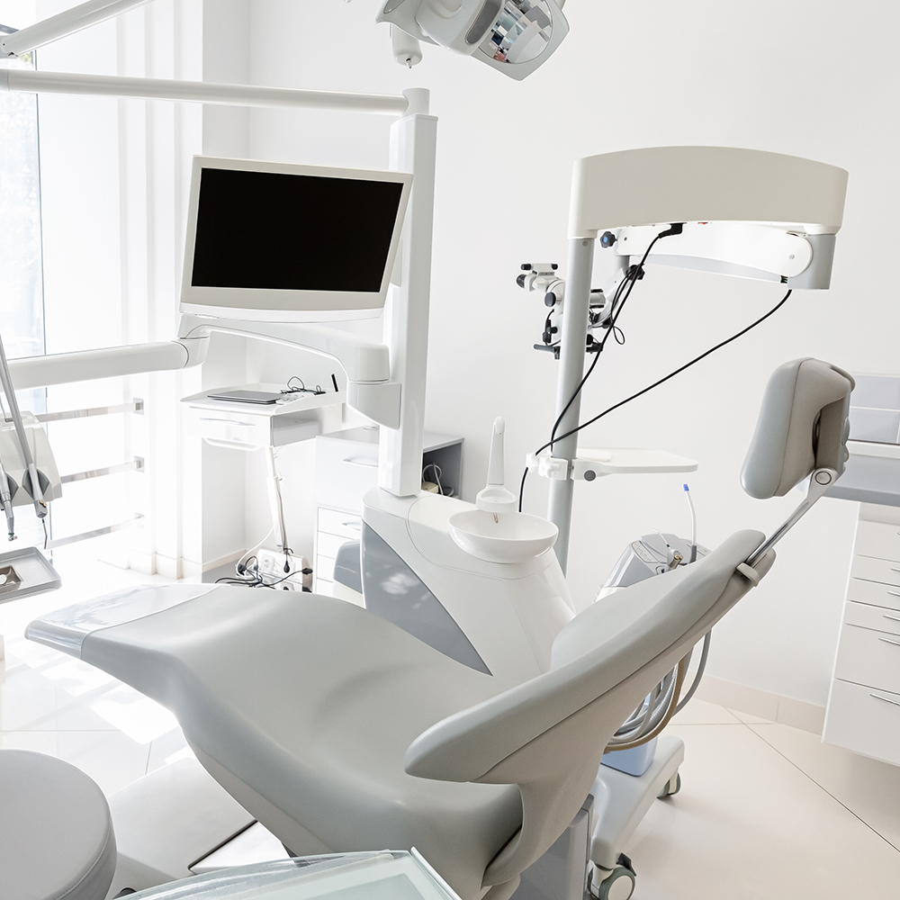 The image shows a modern dental office interior with a chair and dental equipment, including a monitor and a sink, set against a white background.