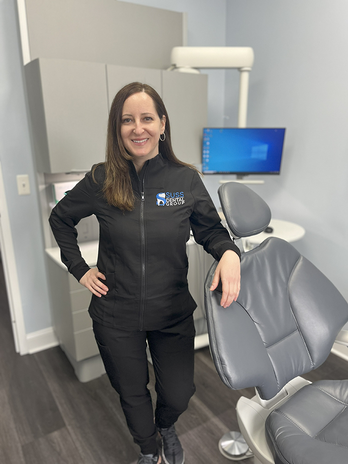 Woman standing in dental office, posing with hands on hips.