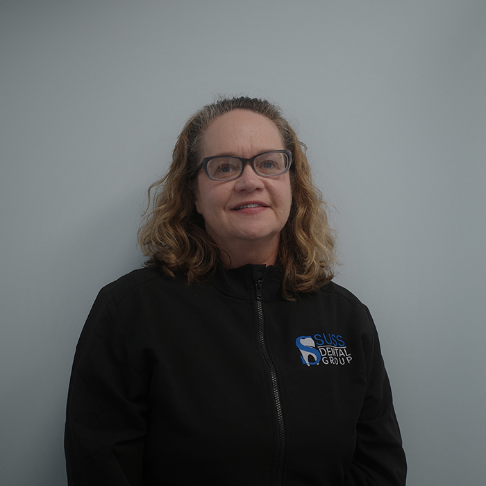 A person standing against a light blue background, wearing glasses and a black jacket with a logo on the left chest area.