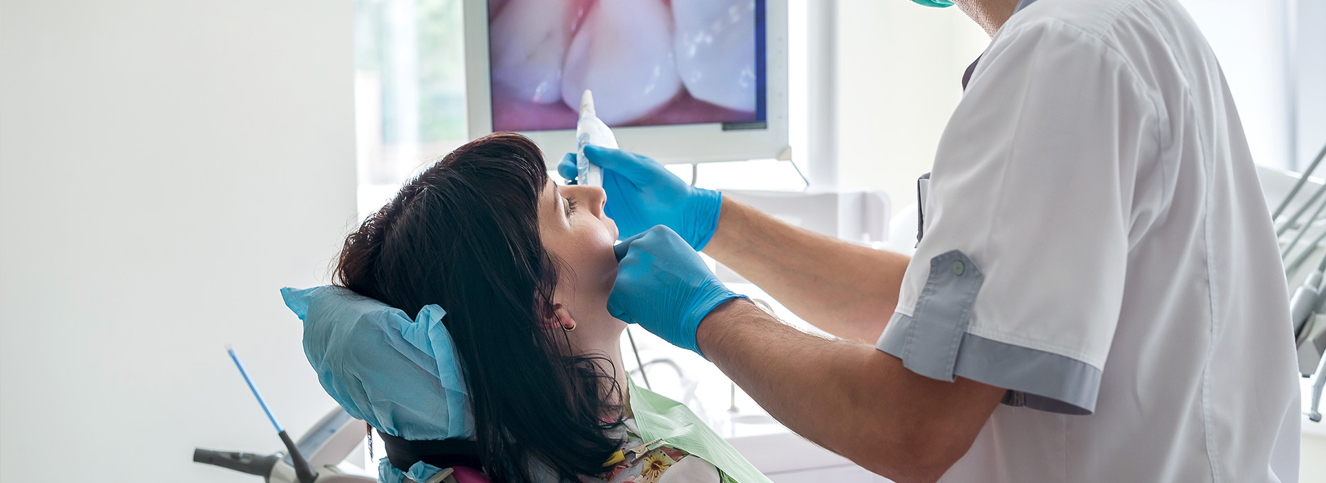 The image shows a dental professional performing an oral procedure on a patient, with the dentist using a dental handpiece and the patient wearing protective eyewear.