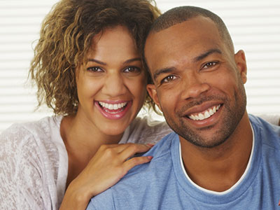 A man and woman posing together with smiles, the man wearing a blue top and the woman with curly hair.