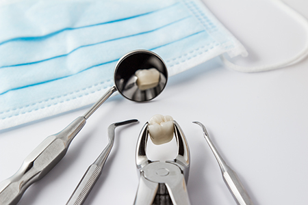 The image shows a collection of dental tools including tweezers, scissors, and a toothbrush, with a focus on a dental mirror being used to inspect a tooth, all set against a blue cloth background.