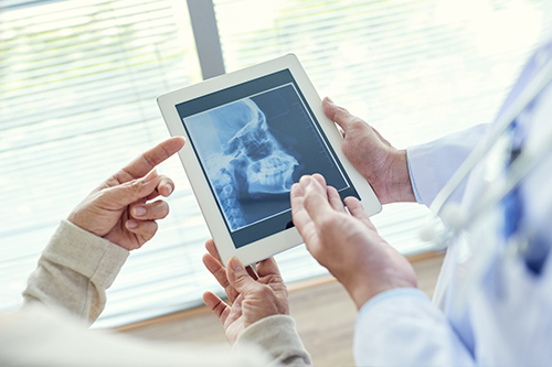 A tablet screen displays a medical X-ray being viewed by two individuals who appear to be healthcare professionals.