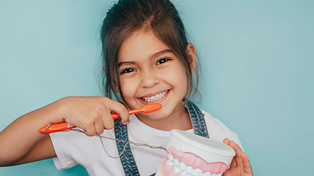 A young girl brushing her teeth with a red toothbrush.