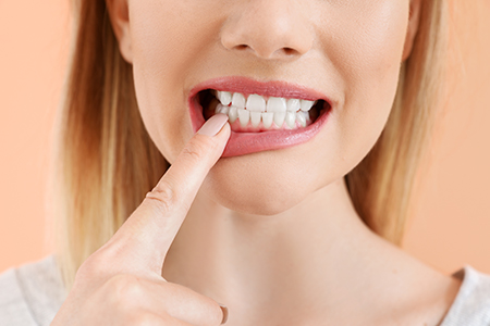 The image shows a close-up of a person with their finger on their teeth, possibly brushing them, against a bright background.