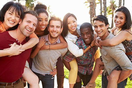 A group of young adults posing together for a photo outdoors during daylight, smiling and embracing each other.