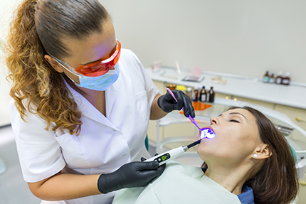 A dental hygienist performing a teeth cleaning procedure on a patient with a mouth open, using an electric toothbrush.