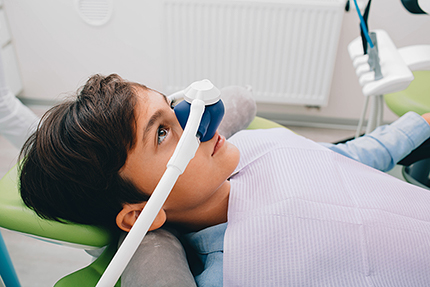 A young person wearing a dental mask and using a dental chair with a headrest for support.